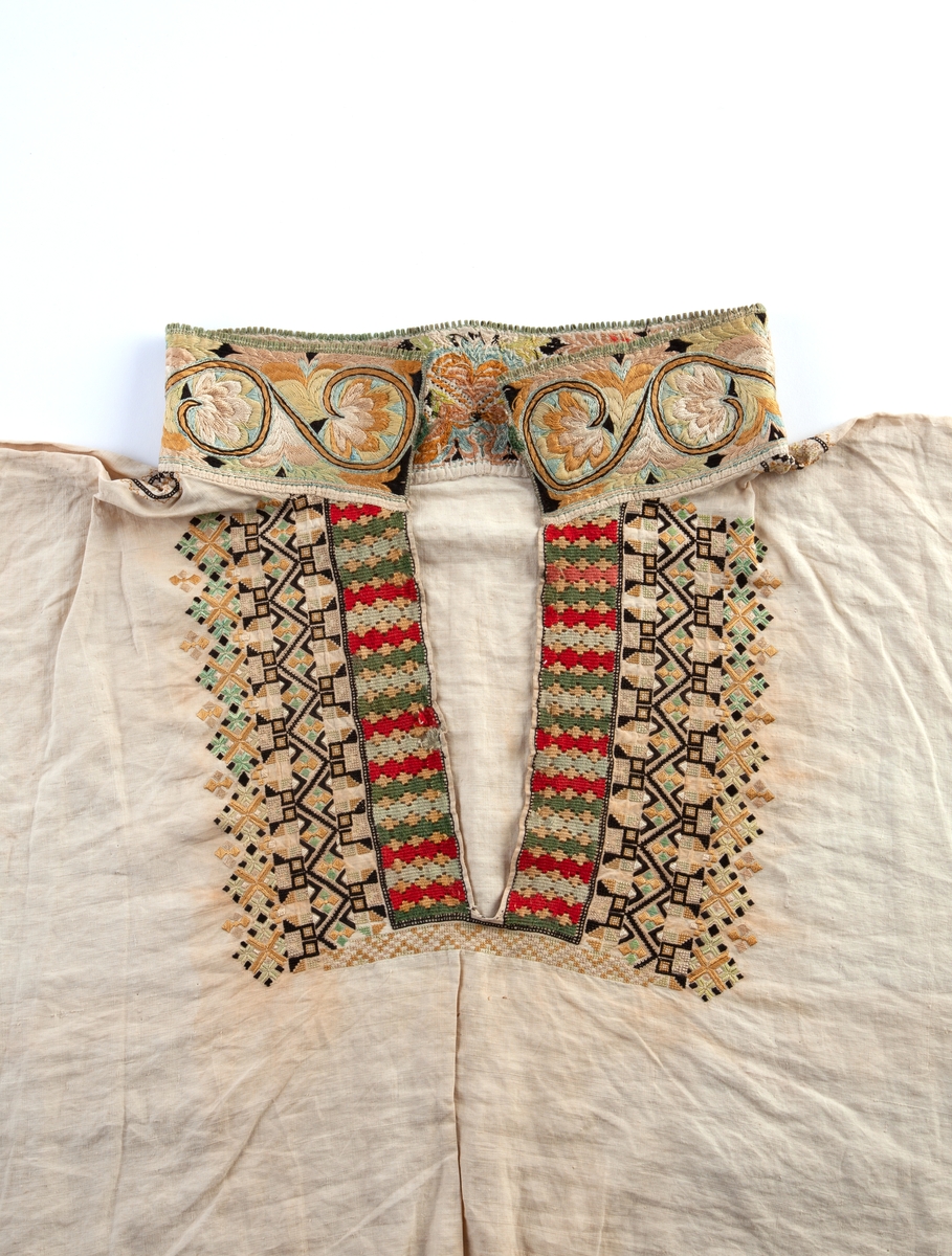 Skjorte fra Sauland, Hjartdal. Broderi på bolen uttrekksøm, klostersøm og korssting. Halslinning og slengerm sydd i plattsøm 
Halskvarde (halslinning) mål:  7,7cm.x57cm ca. Broderi 6,8cm.
Broderi på skulder ca 5,5x6,5cm. 
Brodert bord på slengerm 4cm., avslutning knapphullskant og attersting.