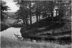 Rumlaborg i Huskvarna med lusthuset på toppen och vattenfylld inre vallgrav. I bakgrunden syns den dåvarande bron över Huskvarnaån och lantliga omgivningar.