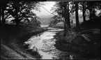 Den inre vallgraven vid Rumlaborg i Huskvarna fotograferad i samband med arkeologiska undersökningar sommaren 1935. Till höger skymtar borgkullen och schakt D1 och D2 som grävdes precis nedanför kullen. I bakgrunden arbetar några män med att skapa en fördämning mot Huskvarnaån. Detta eftersom stockrester som hade grävts fram i vallgraven föregående vinter skulle dokumenteras.