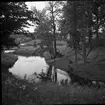 Rumlaborg i Huskvarna. Borgkullen skymtar till höger och vid dess kant står en man vid ett såll.  Den inre vallgraven förbinds med Huskvarnaån. Fotot är taget i samband med arkeologiska undersökningar på platsen sommaren 1938.