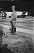 En militär står framför en hangar, 1920-tal. I bakgrunden står en grupp män och samtalar framför en flygplanskropp.