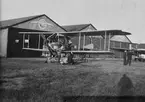 Ett flygplan Thulin C (Albatros SW20) står vid hangarer på Thulins flygskola på Ljungbyhed omkring 1918-1920. Människor i arbete med flygplanet.