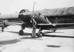 Två flygplan SK 14, märkta F 20-8 och F 20-32 står på flygfält, omkring 1944-1950. Två flygtekniker vid flygplansvinge. Byggnad i bakgrunden.