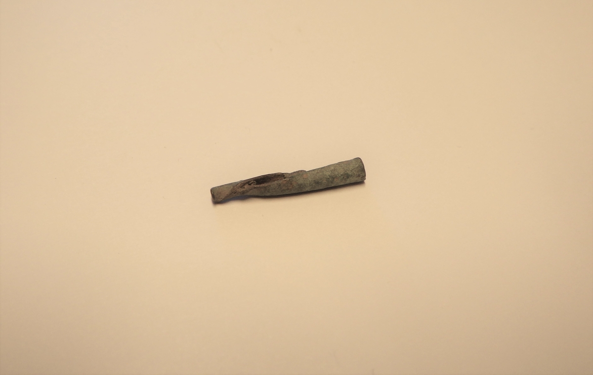 Rest av et lite lissebeslag, dvs en avlang smal metallplate som er krummet på langs slik at den blir et sylinderformet beslag. 