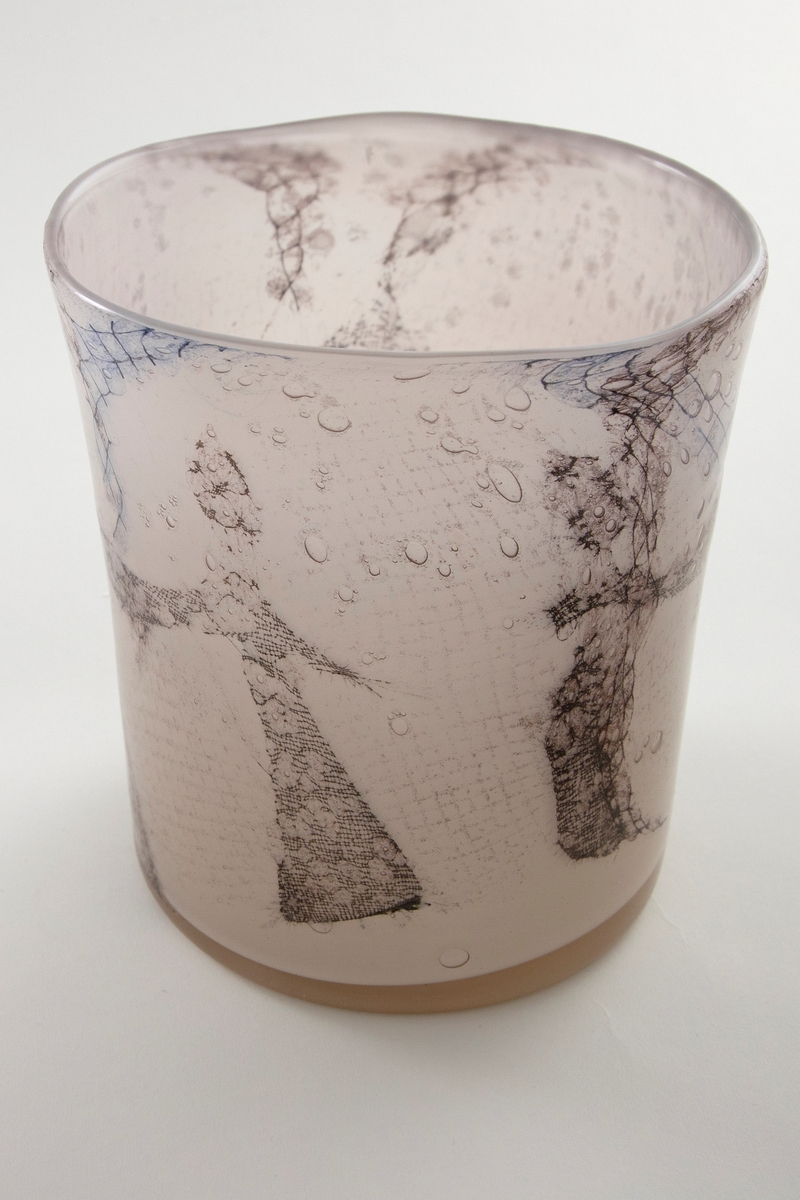 Høyreist ovalformet vase i grårosa glass med innlagt dekor av metallnett. Dekoren fremstiller stiliserte kvinnefigurer i en dansende bevegelse. Øvre del er svakt konisk og har en ujevn formet munningsrand.