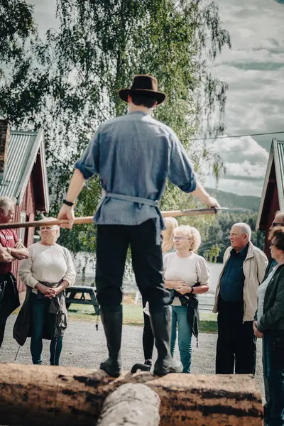 Foto av mann med busserull, hatt og fløterhake som forteller for et publikum