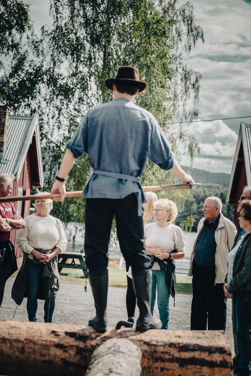 Foto av mann med busserull, hatt og fløterhake som forteller for et publikum