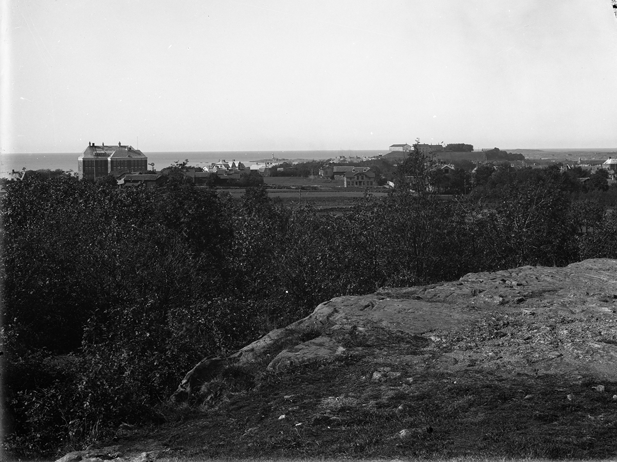 Vy från ett berg mot havet med Varbergs fästning till höger och Södra Folkskolan från 1912, senare Rosenfredsskolan, till vänster. Skrivarklippan med sin fyr skymtar däremellan.