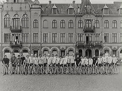 "Cykelklubben Star har en klubbtävling. Cyklisterna har radat upp sig på Varbergs torg framför Stadshotellet. Från vänster: Bertil Karlsson, Gunnar Ottosson, Sixten Bengtsson, Gustav-Adolf Eklund 'Kungen', Nils Nilsson, Gunnar Andersson, Gustav Svensson, Bror Johansson 'Skomakarn' (ägare till 'Brors skor'), Bror Karlsson, Allan Nilsson, Arit Svensson, ?, Gunnar Persson el. Karl-Erik Persson (bröder), Gustav Gustavsson, Erik Andersson 'Kocken', Ernst Andersson, Knut Bernandersson 'Baggen', Sven Liljegren, Åke Johansson, Per Persson, Åke Andreasson 'Skrälla', Göte Blomqvist, Sven Johansson 'Sven J-B', Bror Andersson, Vilhelm Paulsson. OBS klockorna på armen som användes för att kolla tiden. De små är vanliga armbandsklockor medan de större är gamla fickur som man köpt speciella fodral till. De var större och därmed bättre att se tiden på."
