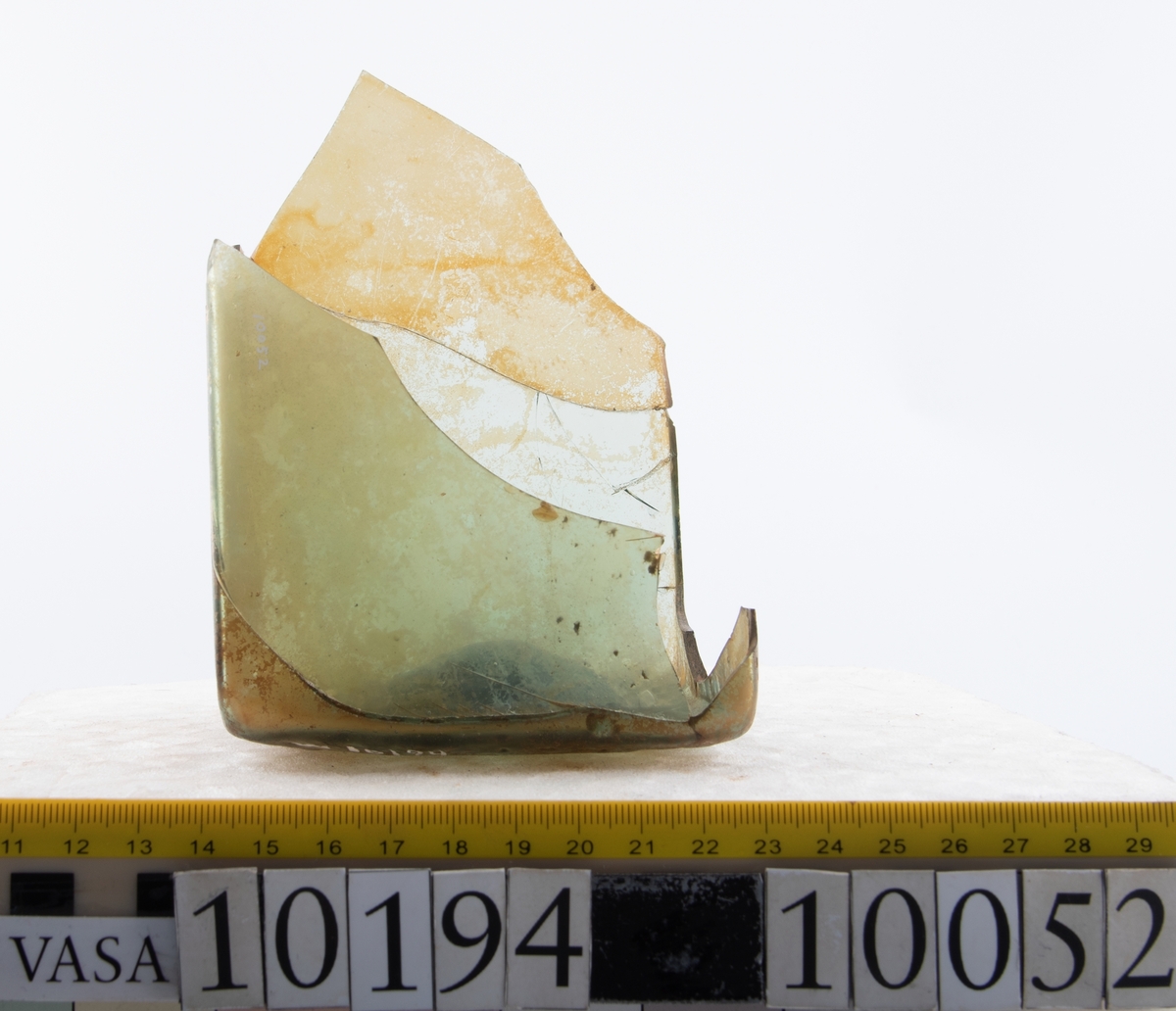 Botten samt fyra skärvor från fyrsidig flaska med stucken botten. På bottnens undersida finns ett puntelmärke. Glaset är grönfärgat och har en iriserande beläggning.

No damage. All pieces are a light green color and are from a case bottle.
10194a: has worn spot
10194c: Consists of two artifact numbers that have been glued together. Artifact has moderate scaling.