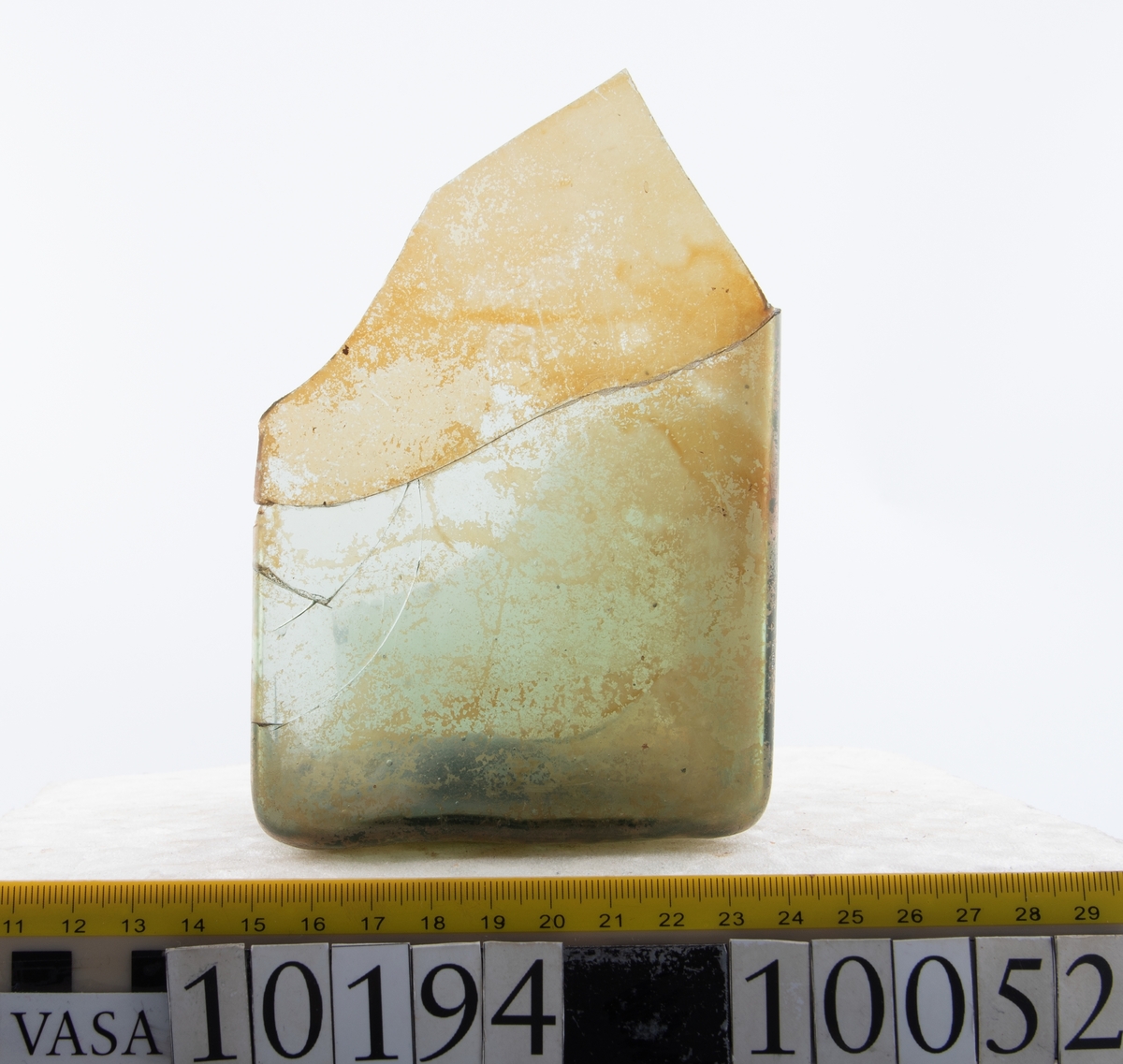 Botten samt fyra skärvor från fyrsidig flaska med stucken botten. På bottnens undersida finns ett puntelmärke. Glaset är grönfärgat och har en iriserande beläggning.

No damage. All pieces are a light green color and are from a case bottle.
10194a: has worn spot
10194c: Consists of two artifact numbers that have been glued together. Artifact has moderate scaling.