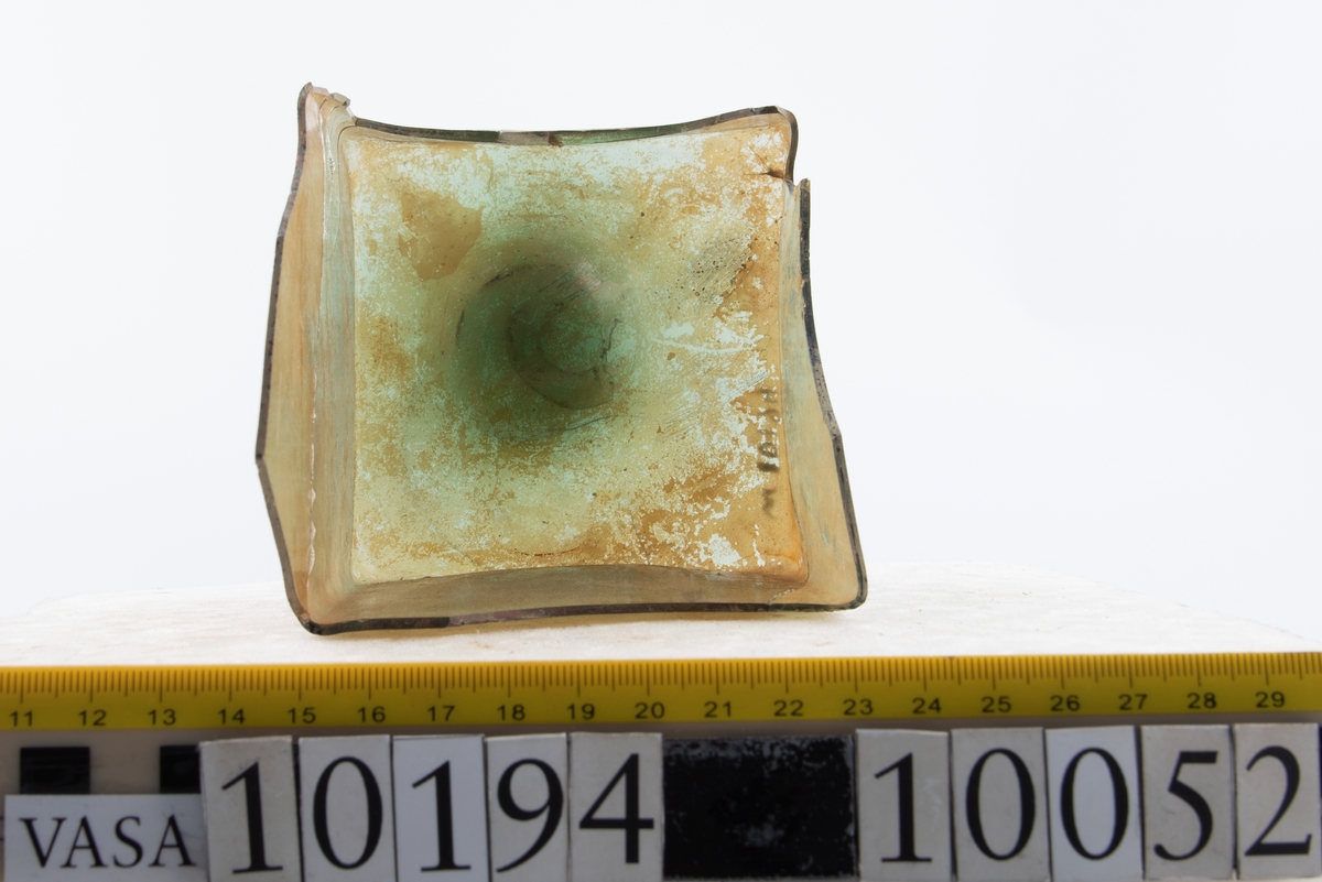 Botten samt fyra skärvor från fyrsidig flaska med stucken botten. På bottnens undersida finns ett puntelmärke. Glaset är grönfärgat och har en iriserande beläggning.

No damage. All pieces are a light green color and are from a case bottle.
10194a: has worn spot
10194c: Consists of two artifact numbers that have been glued together. Artifact has moderate scaling.