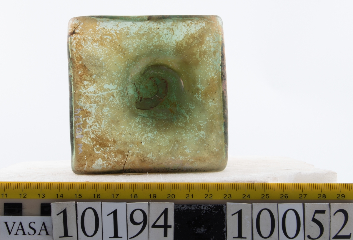 Botten samt fyra skärvor från fyrsidig flaska med stucken botten. På bottnens undersida finns ett puntelmärke. Glaset är grönfärgat och har en iriserande beläggning.

No damage. All pieces are a light green color and are from a case bottle.
10194a: has worn spot
10194c: Consists of two artifact numbers that have been glued together. Artifact has moderate scaling.