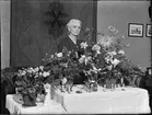 Kvinna i hemmiljö omgiven av blommor, Uppland 1948