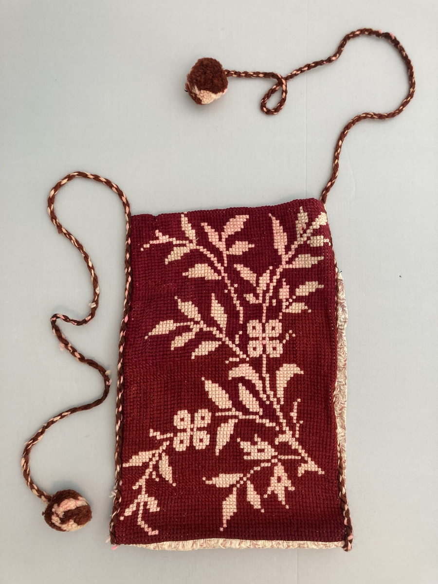 Brev-veske til oppbevaring av post? Sauma i mønstret stoff. På halve stoff-lengda er det sauma på ein brodera del. Dobbel korssting. 2 tvinna gån (garn) med duskar i endane.