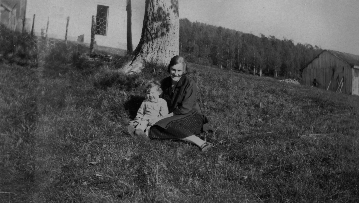 Svanhild og Borghild sitter på gresset foran våningshuset på gården Helstad. Borghild var hushjelp på gården.