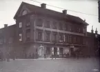 Trots att den så kallade Westmanska gården invid Stora torget i Linköping revs så sent som 1907, har påfallande få fotografier av huvudbyggnaden bevarats för eftervärlden. Här hade den i övrigt så skicklige fotografen Didrik von Essen uppenbara bekymmer med det sena kvällsljuset, men hans vy från 1901 ger oss ändå en god föreställning om hur bebyggelsen i torgets sydvästra del tog sig ut vid tiden. Gatuhuset mot torget torde uppförts kort efter den stora stadsbranden i Linköping år 1700, som för övrigt startade i just denna gård. Gården blev under det sena 1700-talet säte för familjen Westmans blomstrande handelsrörelse och huvudbyggnaden bär tydliga spår av senare utförda om- och tillbyggnader för att bättre passa den förmögna släkten. Vid tiden för bilden ägdes stadsgården ännu av en Westman, den för Linköpings kulturliv så betydelsefulle Henric Westman, men han höll huset uthyrt och bodde själv på sin gård Valla väster om staden. I gatuplanet drevs i det centralt belägna huset som brukligt handel. Störst yta upptogs av AB Sundquists & Co, en snus- och tobaksaffär som drevs av änkefru Mathilda Ekström. I husets andra ände hade Tannefors Nya Valskvarn handel med mjöl, gryn och torrjäst, men plats gavs även för systrarna Lovisa Charlotta och Johanna Augusta Johanssons kaffeservering. I den storslagna montern mot hörnet av Bokhållaregatan gjorde fotografen Swen Swenssons reklam för sina alster. Gården revs 1907 för att ge plats för det så kallade Centralpalatset.