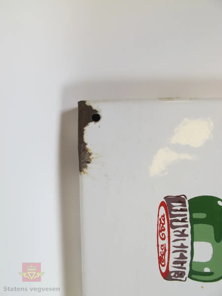 Hovedsakelig rødt og hvitt emaljeskilt laget av metall. Det er et skruehull i hvert hjørne og rust rundt to av disse.