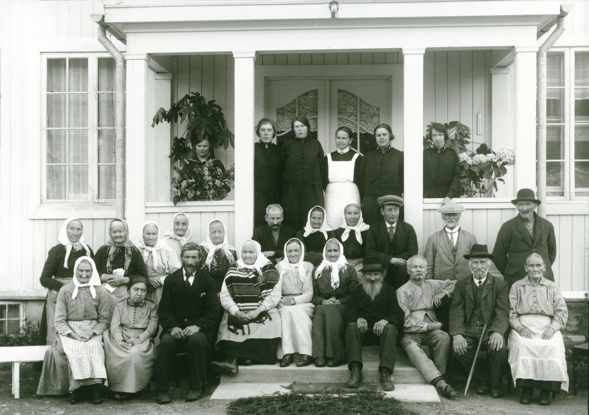 27 personer fotografert på trappa på Gammelhjemmet (Nordhagen).1. rekke fra venstre: Ukjent, Ida Kjærnmoen (1893-1986), Halvor Buflod "Bilo" (1870-1957), ant. Elisabeth Toll, Pernille Søberg, ukjent, Ener Mortensen Skjærberget "Kimmern"* (1843-1930), 3 ukjente. 2. rekke fra venstre: Ukjent, Pernille Buflod f. Sandkveen (1834-1935), 2 ukjente, Kerste Smørmyren f. Mehagen (1844-1938), 3 ukjente, Johan Bekken (1894-1942), Kristian Trolsberget (1856-1936), Amund Buflod (1846-1936) eller Martin Gundersen Grinda. 3. rekke fra venstre: Margit Løvbrenden (1904-1987) (pige på Gammelhjemmet), ukjent, Odlaug Lindberget g. Flermoen (1906-1976), Kari Wolen (1881-1971) (bestyrerinne), Pauline Søberg f. Normann eller Bergljot Holt g. Solberg, Paula Djupvik (1904-1991).