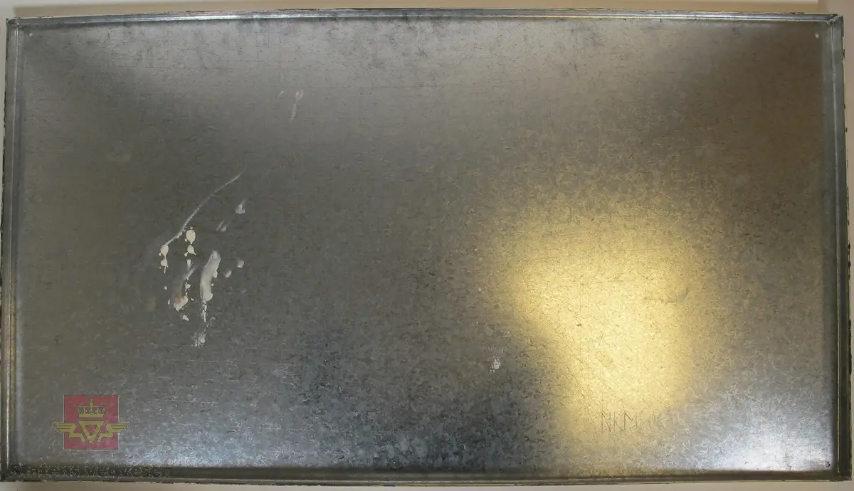 Rektangulært skilt lagd av metall, med teksten "P. Helleberg" med svarte og "Vognmand" med røde bokstaver på hvit/brun bakgrunn. Det er laget et hull i hvert av hjørnene.