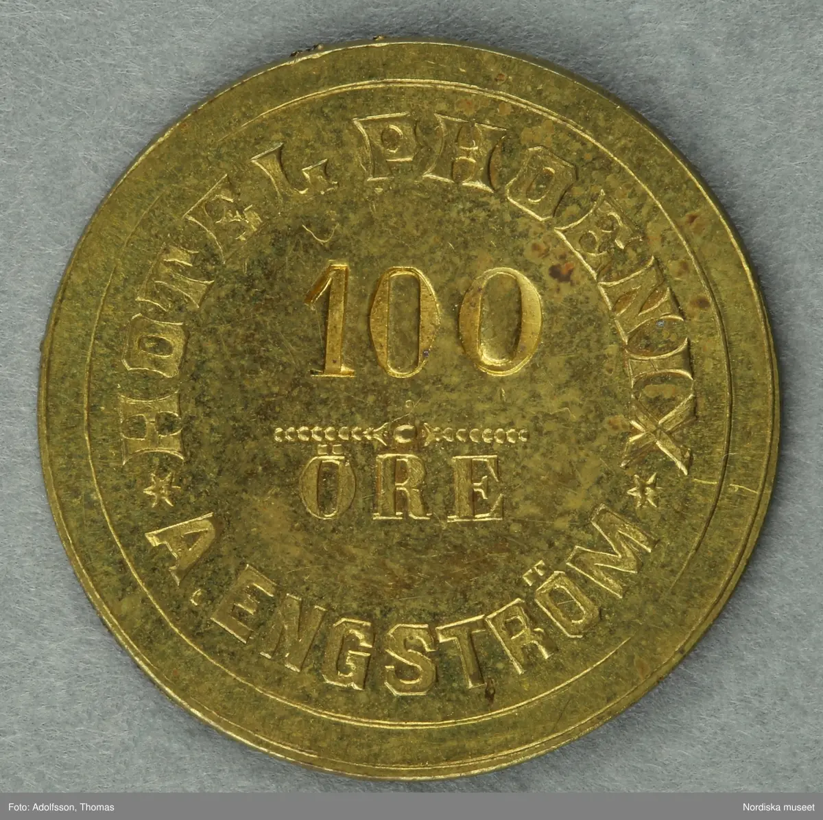 Huvudliggaren:
"Pollett, restaurangpollett; mässing, rund; åtsidan '100' och 'öre', samt 'HOTEL PHOENIX A ENGSTRÖM'; frånsidan 'C C Sporrong & Co Stockholm'; Hotel Phoenix, Stockholm. Ciam 2,8 cm. [Tillverkare] C C Sporrong & Co, Sthlm.
G. 1/4 1970 Direktör Tore Wretman, Stockholm."
