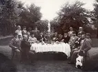 Sällskapet Lördagsbröderna samlade i trädgården hos kassör Karl Berg men oaktat namnet hölls just denna samling onsdagen den 21 augusti 1895. Vid sidan av värden ser vi följande bröder: Redaktionssekreterarna Karl Lindh och August Billsten, bokhållarna Axel Ajaxson, August Neuman och Johan Ekvall. Vidare läroverksadjunkt Axel Kristofersson, bankkassör Hjalmar Svensson, apotekare Karl Sandsjoe och postkontrollör Erik Lindh. Till höger om värden följer telegrafkommissarie Per Egnell, landskontorist Anders Boström, hypoteksbokhållare Gustaf Gustavi, apotekare Karl Stridner, postexpeditör Knut Berg, bokhållare Robert Dahlgren och kamrer Bengt Orre samt trädgårdsdirektör Victor Holm med sin trogne jaktkamrat hunden Dido.