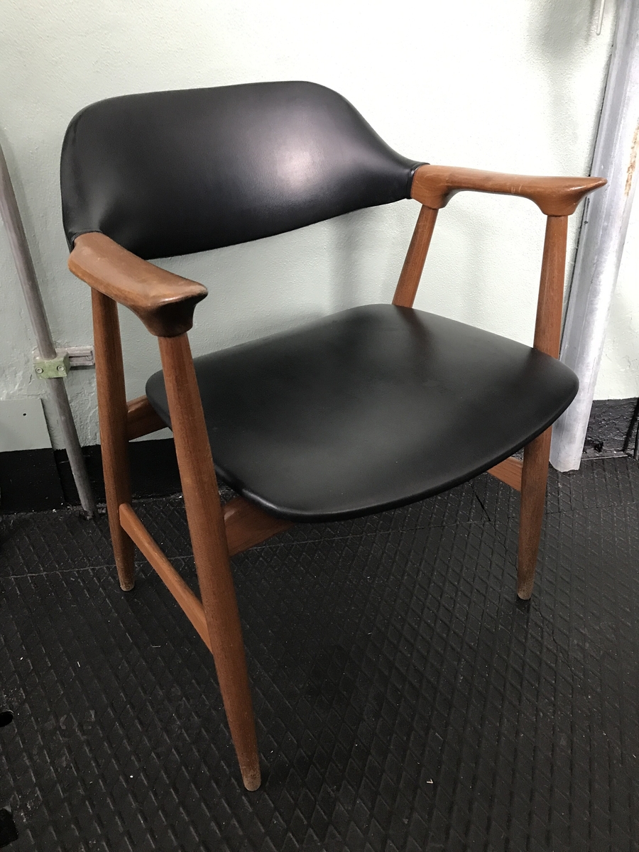 Lett armstol i teak treverk med sete og rygg av svart skai. Armlenet er svakt bua i lengderetninga og spissa mot front og har eit elegant og lett uttrykk.  Akterstavar/bakbein og frambein er festa i armlenene, der også ryggbrettet er festa. Tverrtre framme og bak under setet og tverrtre mellom for- og bakbein. Ryggbrettet er bua på toppen. Setet er svakt bua i framkant og litt meir i bakkant. Stolen er sterkt prega av vaskeslitasje rundt stolbeina og misfarging i treverket særleg på armlenene. 
