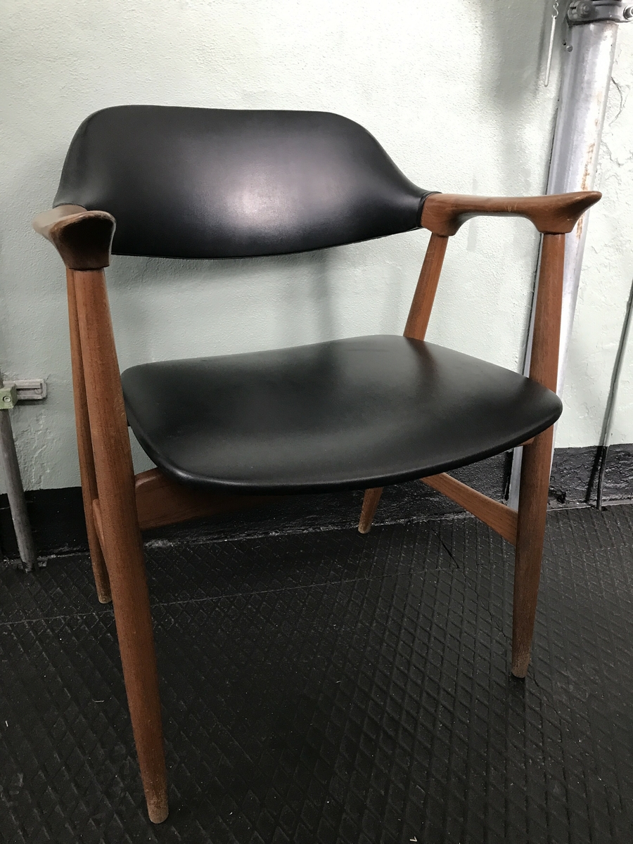 Lett armstol i teak treverk med sete og rygg av svart skai. Armlenet er svakt bua i lengderetninga og spissa mot front og har eit elegant og lett uttrykk.  Akterstavar/bakbein og frambein er festa i armlenene, der også ryggbrettet er festa. Tverrtre framme og bak under setet og tverrtre mellom for- og bakbein. Ryggbrettet er bua på toppen. Setet er svakt bua i framkant og litt meir i bakkant. Stolen er sterkt prega av vaskeslitasje rundt stolbeina og misfarging i treverket særleg på armlenene. 