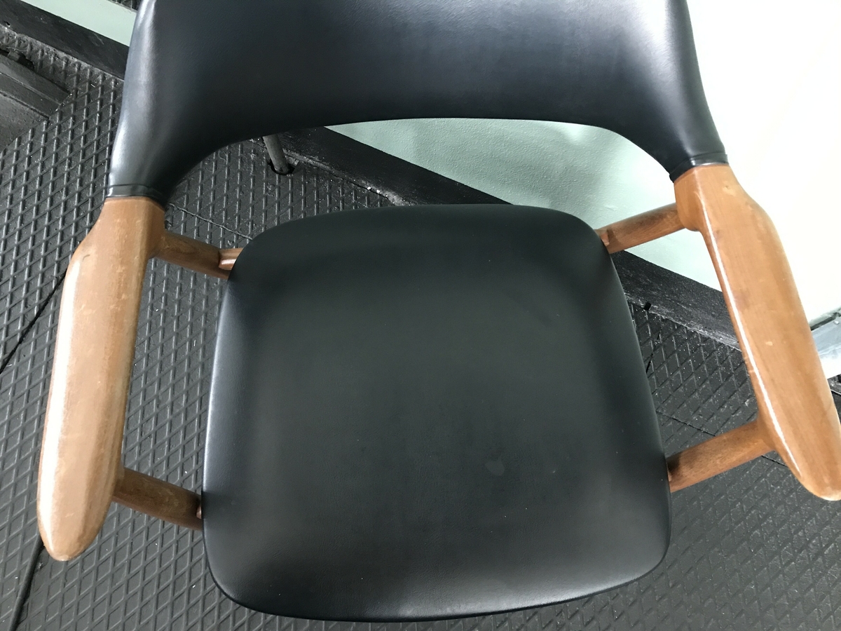 Lett armstol i teak treverk med sete og rygg av svart skai. Armlenet er svakt bua i lengderetninga og spissa mot front og har eit elegant og lett uttrykk.  Akterstavar/bakbein og frambein er festa i armlenene, der også ryggbrettet er festa. Tverrtre framme og bak under setet og tverrtre mellom for- og bakbein. Ryggbrettet er bua på toppen. Setet er svakt bua i framkant og litt meir i bakkant. Stolen er sterkt prega av vaskeslitasje rundt stolbeina og misfarging i treverket særleg på armlenene. 