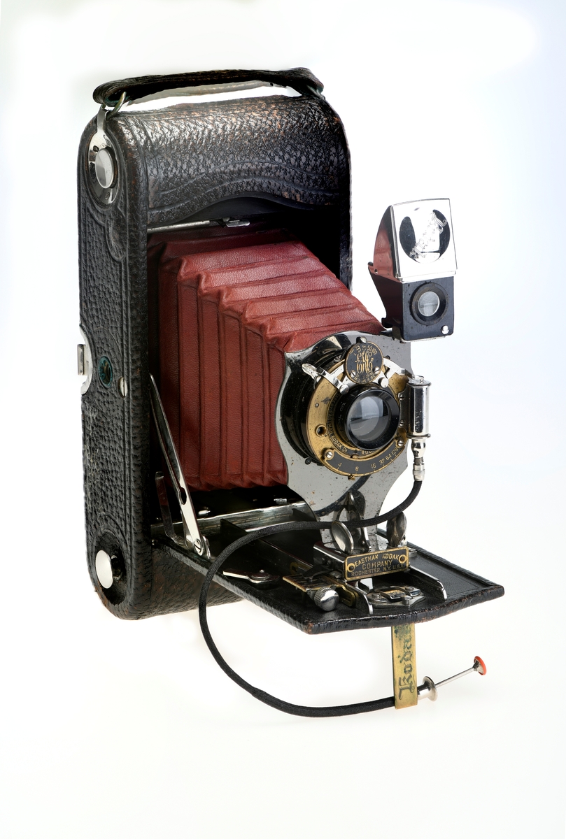 Et belgkamera for 116-film fra Kodak. No. 1A Folding pocket ble laget i flere versjoner mellom 1899 og 1915 og var det første kameraet fra Kodak til å bruke 116-film. Av de fire versjonene (Model A, B, C, D) var denne Model D den første til å ha en objektivplate i metall, mens de tidligere versjonene hadde en objektivplate i tre. 

Kameraet tar bilder på 6,5x11 cm. Det har 3 lukkertider i tillegg til åpen lukker (B). I tillegg til lukkeren på objektivet har kameraet også en snorutløser. På skinnen som belgen er festet i er det et lite hjul for å stoppe belgen i ulike posisjoner merket med fokusavstand. Det er en søker foran på objektivplaten som kan roteres for å ta landskapsbilder, og søkeren har et deksel som kan vippes opp. Baksiden kan åpnes for å sette inn film, og det har et rødt vindu for å se om det er film i. Luken til belgen åpnes med en knapp på siden av kameraet, på luken er det en fot som kan brettes ut. Håndtak i skinn på toppen. Kameraet kommer i en veske av skinn. Med kameraet følger også en mekanisk opptrekkbar selvutløser som kan festes på enden av snorutløseren.