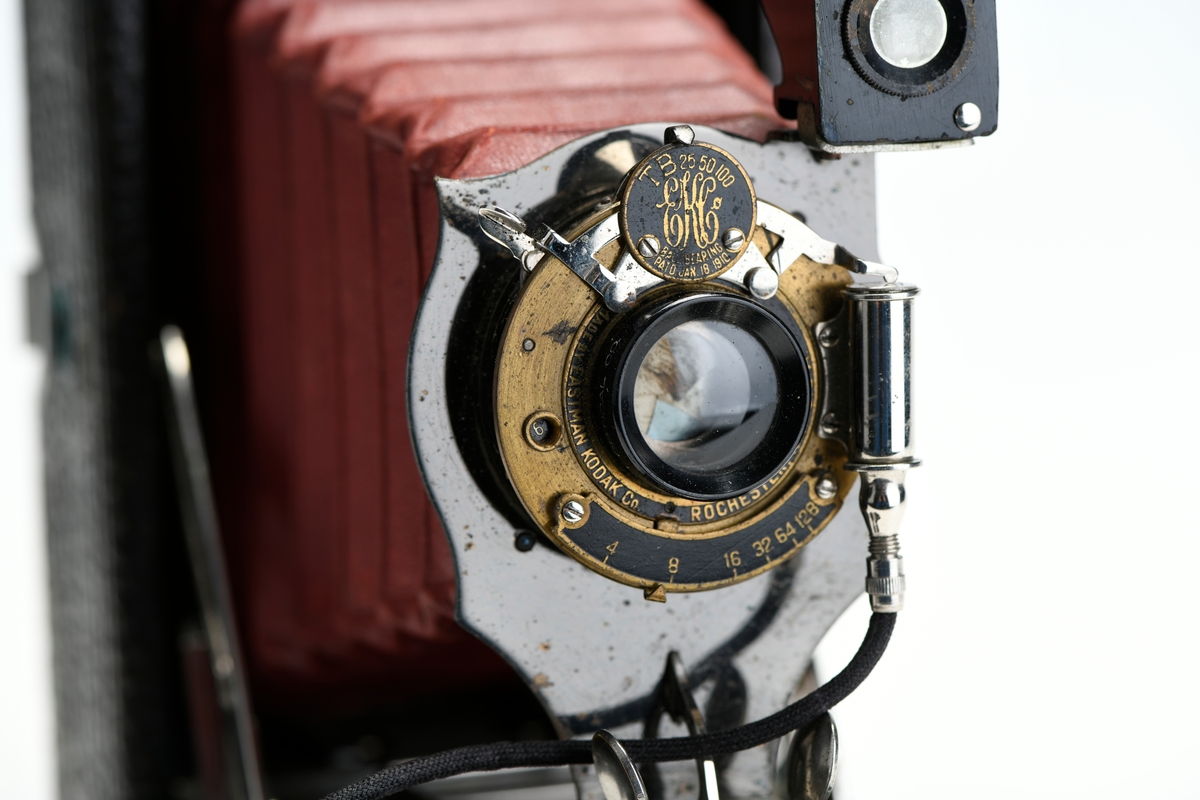 Et belgkamera for 116-film fra Kodak. No. 1A Folding pocket ble laget i flere versjoner mellom 1899 og 1915 og var det første kameraet fra Kodak til å bruke 116-film. Av de fire versjonene (Model A, B, C, D) var denne Model D den første til å ha en objektivplate i metall, mens de tidligere versjonene hadde en objektivplate i tre. 

Kameraet tar bilder på 6,5x11 cm. Det har 3 lukkertider i tillegg til åpen lukker (B). I tillegg til lukkeren på objektivet har kameraet også en snorutløser. På skinnen som belgen er festet i er det et lite hjul for å stoppe belgen i ulike posisjoner merket med fokusavstand. Det er en søker foran på objektivplaten som kan roteres for å ta landskapsbilder, og søkeren har et deksel som kan vippes opp. Baksiden kan åpnes for å sette inn film, og det har et rødt vindu for å se om det er film i. Luken til belgen åpnes med en knapp på siden av kameraet, på luken er det en fot som kan brettes ut. Håndtak i skinn på toppen. Kameraet kommer i en veske av skinn. Med kameraet følger også en mekanisk opptrekkbar selvutløser som kan festes på enden av snorutløseren.