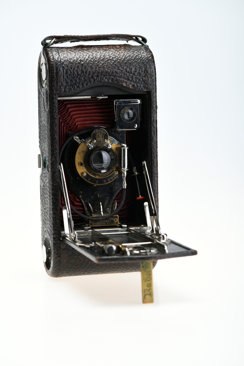 Et belgkamera for 116-film fra Kodak. No. 1A Folding pocket ble laget i flere versjoner mellom 1899 og 1915 og var det første kameraet fra Kodak til å bruke 116-film. Av de fire versjonene (Model A, B, C, D) var denne Model D den første til å ha en objektivplate i metall, mens de tidligere versjonene hadde en objektivplate i tre. 

Kameraet tar bilder på 6,5x11 cm. Det har 3 lukkertider i tillegg til åpen lukker (B). I tillegg til lukkeren på objektivet har kameraet også en snorutløser. På skinnen som belgen er festet i er det et lite hjul for å stoppe belgen i ulike posisjoner merket med fokusavstand. Det er en søker foran på objektivplaten som kan roteres for å ta landskapsbilder, og søkeren har et deksel som kan vippes opp. Baksiden kan åpnes for å sette inn film, og det har et rødt vindu for å se om det er film i. Luken til belgen åpnes med en knapp på siden av kameraet, på luken er det en fot som kan brettes ut. Håndtak i skinn på toppen. Kameraet kommer i en veske av skinn. Med kameraet følger også en mekanisk opptrekkbar selvutløser som kan festes på enden av snorutløseren.