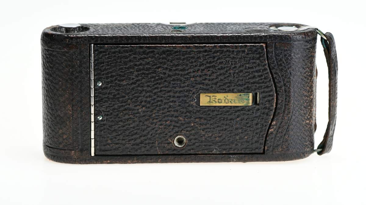 Et belgkamera for 116-film fra Kodak. No. 1A Folding pocket ble laget i flere versjoner mellom 1899 og 1915 og var det første kameraet fra Kodak til å bruke 116-film. Av de fire versjonene (Model A, B, C, D) var denne Model D den første til å ha en objektivplate i metall, mens de tidligere versjonene hadde en objektivplate i tre. 

Kameraet tar bilder på 6,5x11 cm. Det har 3 lukkertider i tillegg til åpen lukker (B). I tillegg til lukkeren på objektivet har kameraet også en snorutløser. På skinnen som belgen er festet i er det et lite hjul for å stoppe belgen i ulike posisjoner merket med fokusavstand. Det er en søker foran på objektivplaten som kan roteres for å ta landskapsbilder, og søkeren har et deksel som kan vippes opp. Baksiden kan åpnes for å sette inn film, og det har et rødt vindu for å se om det er film i. Luken til belgen åpnes med en knapp på siden av kameraet, på luken er det en fot som kan brettes ut. Håndtak i skinn på toppen. Kameraet kommer i en veske av skinn. Med kameraet følger også en mekanisk opptrekkbar selvutløser som kan festes på enden av snorutløseren.