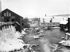 Motiv från Boxholms bruk 1903. Vy från Sågbron mot brukets sågverk och kvarn. Långt nedströms syns landsvägsbron och takåsar vid det så kallade Nedre verket. På spårvägsbron i bildens mitt fraktades spån till Sågspånshuset vars takås skymtar längst till höger.