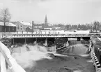 Motiv från Boxholm 1897. I förgrunden Sågbron över Sågfallet. I bakgrunden till vänster brukets snickerifabrik och i fonden ortens kyrka.