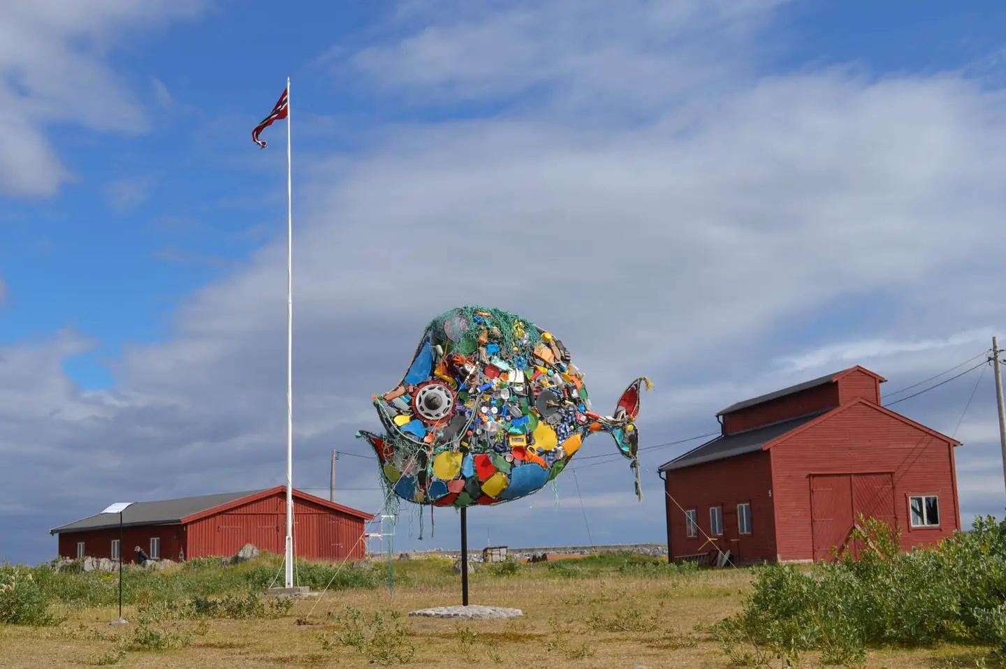 Utendørs om sommeren, en fiskeskulptur og Berlevåg Havnemuseum.