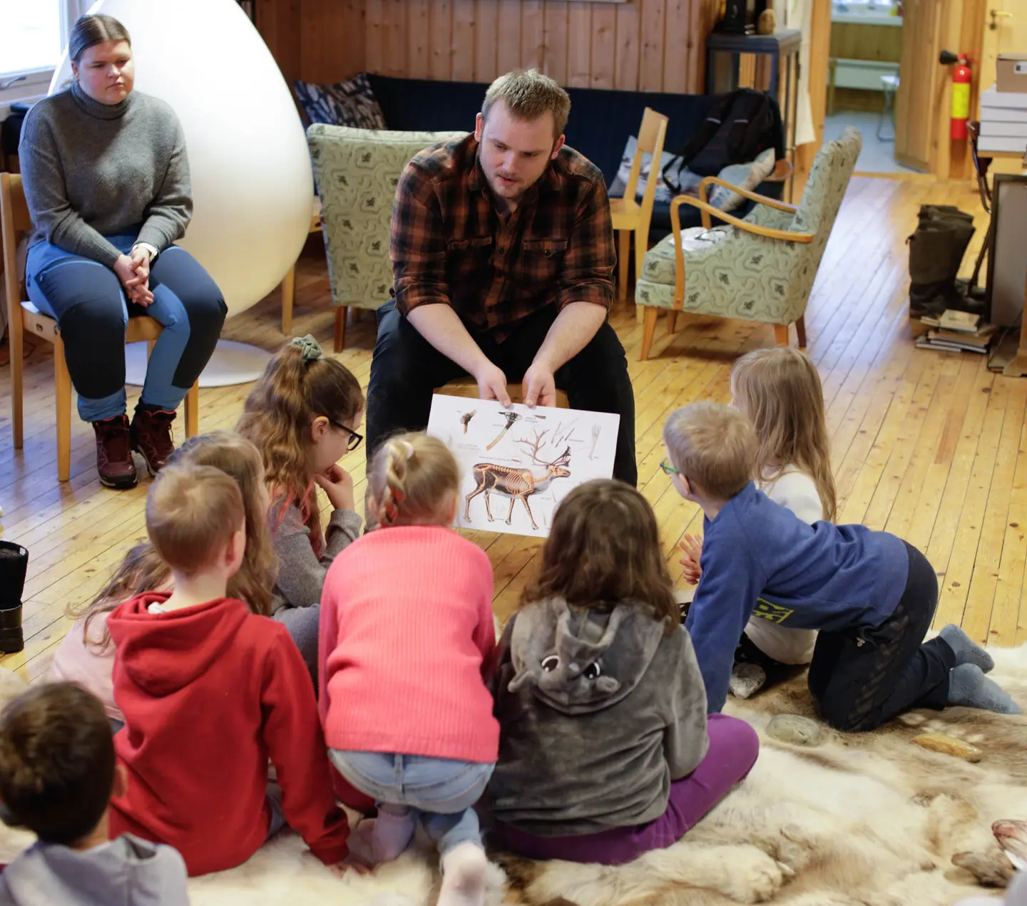 En mann sitter sammen med barn på museet. De ser på et bilde av en rein.