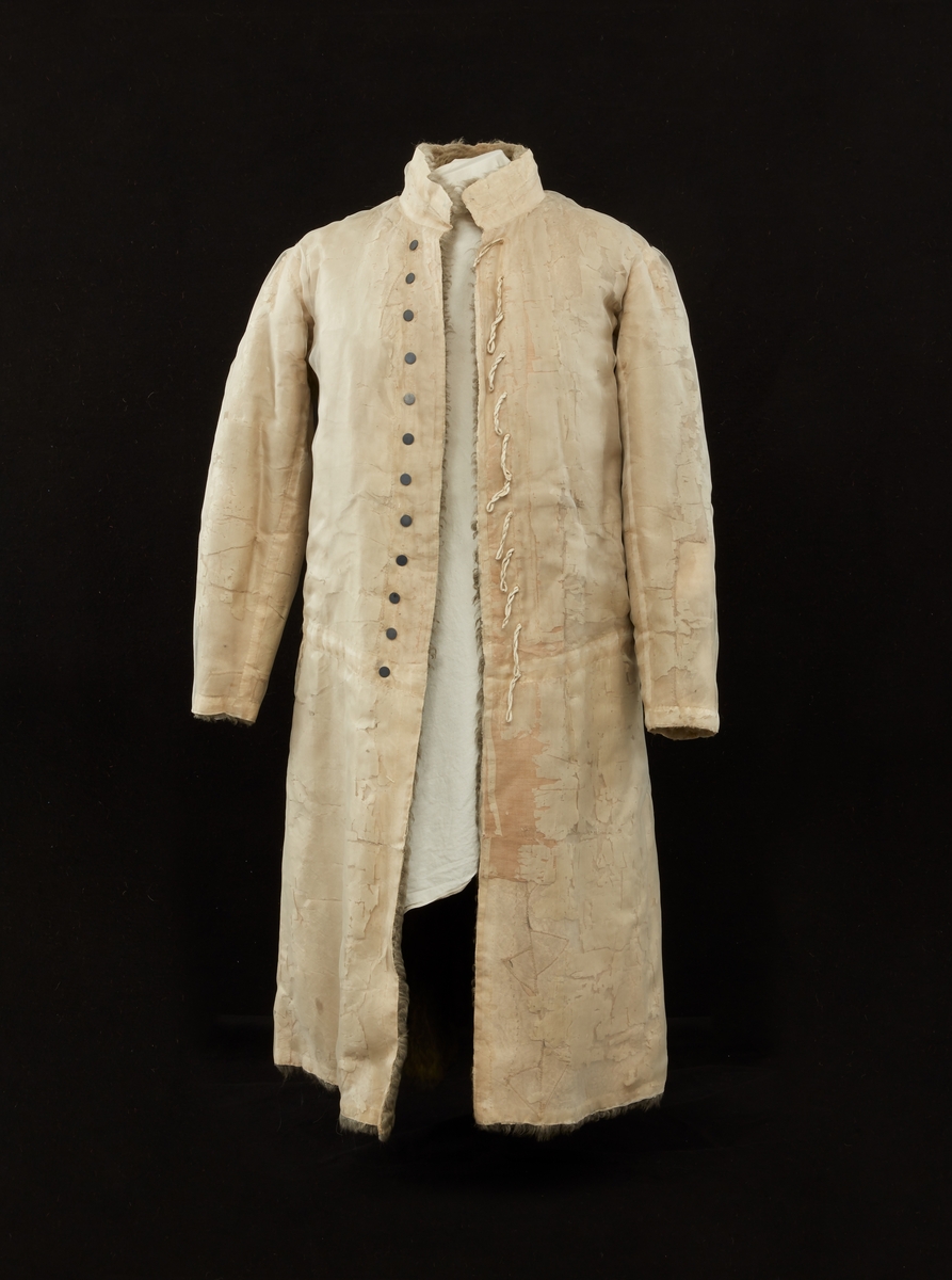 Skinnpäls tillhörande Gustav III:s daluniform. Långpäls av vita lammskinn, klädd med vit sidensars. Snitt som DM 110-111, men med smalt midjeband samt utan ärmuppslag. Knäppt åt höger med 12 små silverknappar och hyskor av skinn.
