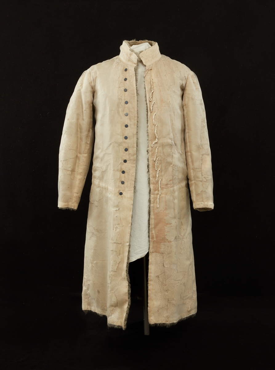 Skinnpäls tillhörande Gustav III:s daluniform. Långpäls av vita lammskinn, klädd med vit sidensars. Snitt som DM 110-111, men med smalt midjeband samt utan ärmuppslag. Knäppt åt höger med 12 små silverknappar och hyskor av skinn.