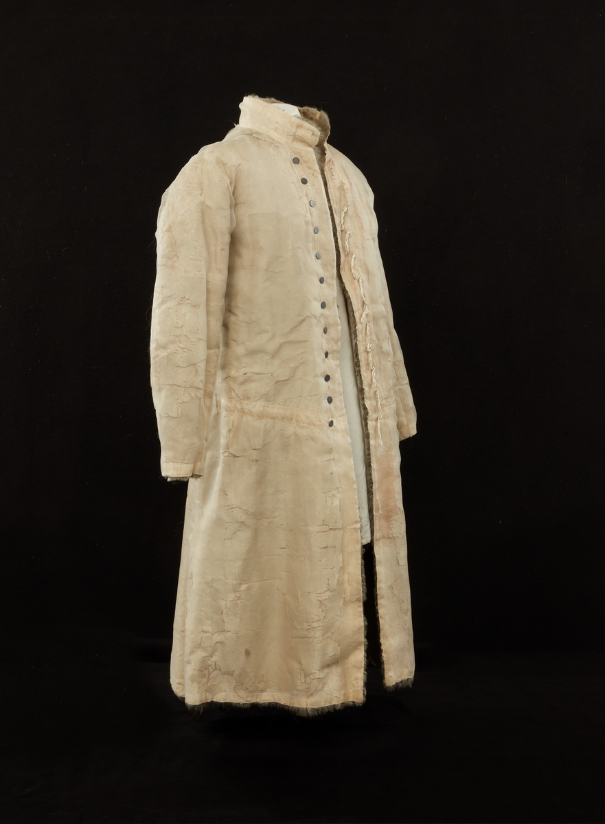 Skinnpäls tillhörande Gustav III:s daluniform. Långpäls av vita lammskinn, klädd med vit sidensars. Snitt som DM 110-111, men med smalt midjeband samt utan ärmuppslag. Knäppt åt höger med 12 små silverknappar och hyskor av skinn.