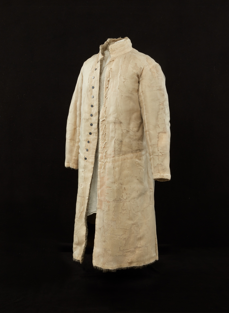 Skinnpäls tillhörande Gustav III:s daluniform. Långpäls av vita lammskinn, klädd med vit sidensars. Snitt som DM 110-111, men med smalt midjeband samt utan ärmuppslag. Knäppt åt höger med 12 små silverknappar och hyskor av skinn.