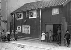 Linköpingsfotografen Didrik von Essen väckte uppmärksamhet bland boende utmed Hunnebergsgatan när han passerade en sommardag 1903. Gatuskylten ger besked om att han stannat vid Hunnebergsgatan 16 A, som vid tiden ägdes av resepredikanten Johan Ludvig Norman. Den handskrivna skylten till höger med texten No 59, talar upplysningsvis om att gården låg efter dåtidens kvatersindelning i Sankt Pers kvarter nr 59. I övrigt är huset ett exempel på den enkla träkåksbebyggelse som ännu vid tiden för bilden var gängse bostad för många mindre bemedlade stadsbor.