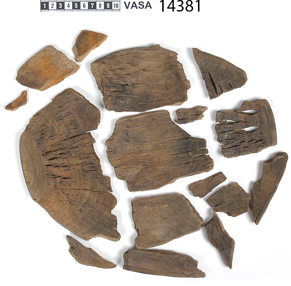 En träskål i delar.

Av delarna att döma har skålen varit plant samt försett med en svarvad fotring. På insidan av skålen, strax nedanför mynningskanten, har det löpt en dekorativ, svarvad linje. Mindre bitar av skålen saknas.

Delarna är mycket spruckna och mycket sköra.