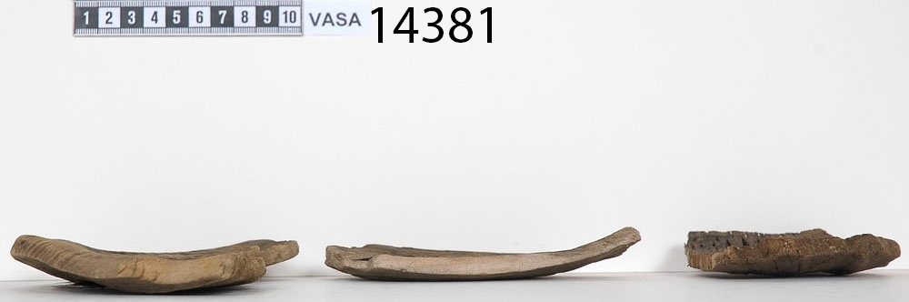 En träskål i delar.

Av delarna att döma har skålen varit plant samt försett med en svarvad fotring. På insidan av skålen, strax nedanför mynningskanten, har det löpt en dekorativ, svarvad linje. Mindre bitar av skålen saknas.

Delarna är mycket spruckna och mycket sköra.