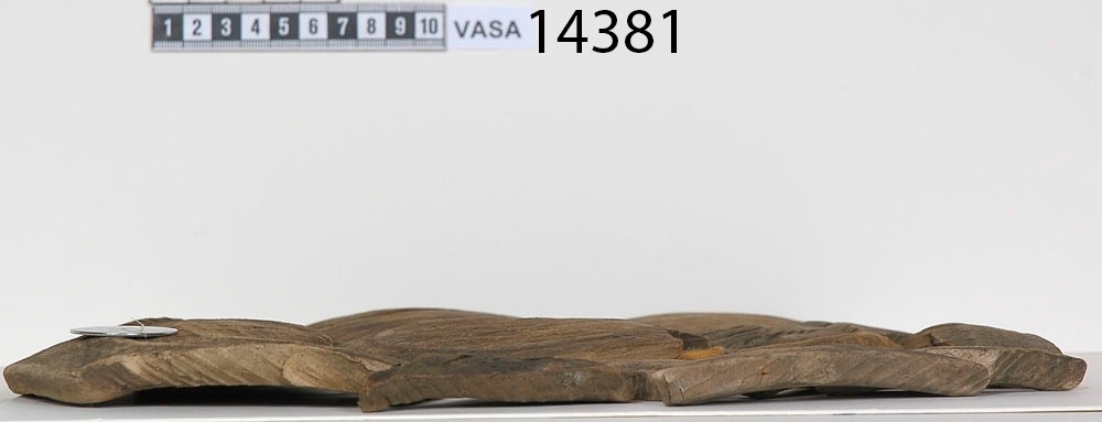 En träskål i delar.

Av delarna att döma har skålen varit plant samt försett med en svarvad fotring. På insidan av skålen, strax nedanför mynningskanten, har det löpt en dekorativ, svarvad linje. Mindre bitar av skålen saknas.

Delarna är mycket spruckna och mycket sköra.