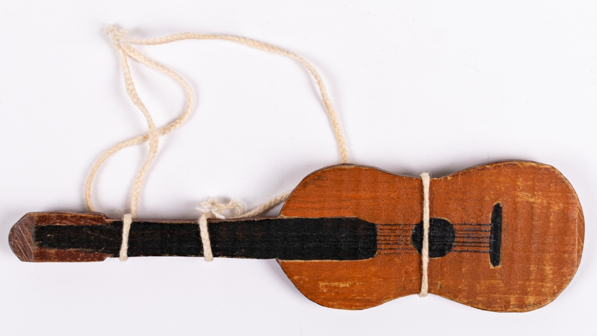 Liten gitarr tillhörande dockteater. Brun med svart hals och vitt snöre runt.