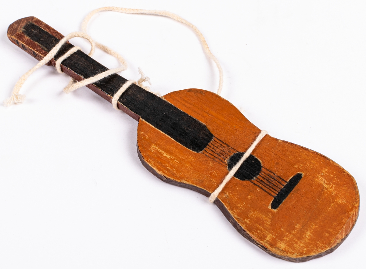 Liten gitarr tillhörande dockteater. Brun med svart hals och vitt snöre runt.