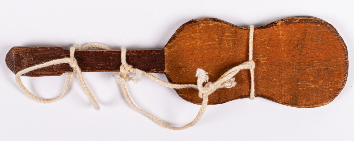 Liten gitarr tillhörande dockteater. Brun med svart hals och vitt snöre runt.