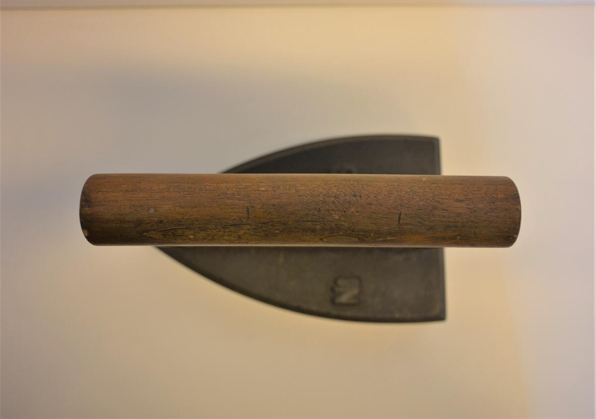 Strykjärn. Fot av massivt järn. Stämplad No 6. Med två skruvar fastsatt handtag av järn, bandjärn, grepp av en björkstav. Stämplad HUSQVARNA. Gåva: Hans och Gerda Nybergs dödsbo, Härnösand, 11/6 1977. 
