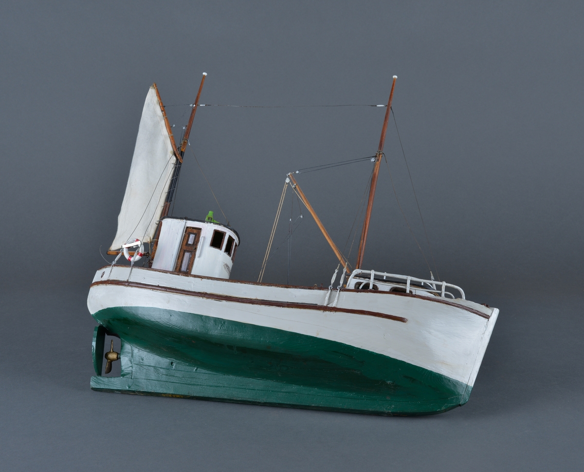 Fiskebåt eller sjark laget i trevirke. Båtmodellen står på et stativ laget av mørkt tre, antatt teak. Støttene har utskjæringer. 
Båten har styrhus, nedgang til lugarene i baugen. Mast foran med bom og messanmast med gaffelsegl.